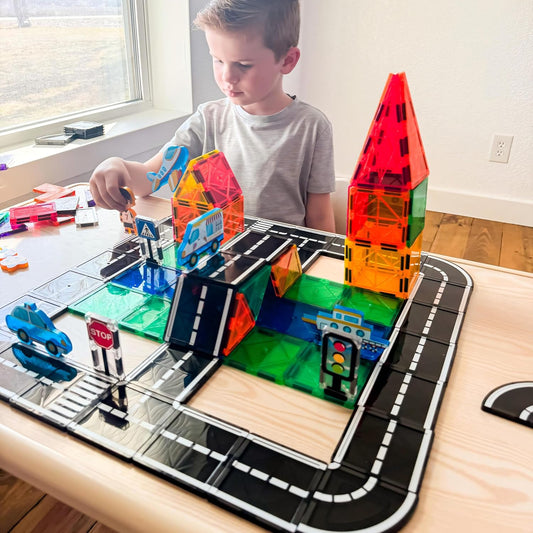 Magnetic tile city with road pieces, traffic signs and toy cars on a play mat